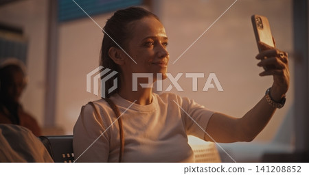 Young Female Passenger Using Smartphone for Video Conversation in Airport Lounge Young Female Passenger Using Smartphone for Video Conversation in Airport Lounge 141208852
