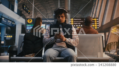 Young Male Traveler with Headphones Using Smartphone and Taking Selfie at Airport Young Male Traveler with Headphones Using Smartphone and Taking Selfie at Airport 141208880