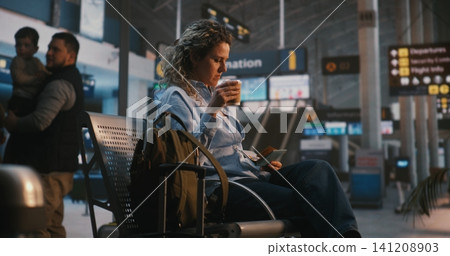 Woman Checking Flight Details and Drinking Coffee in Airport Lounge Woman Checking Flight Details and Drinking Coffee in Airport Lounge 141208903