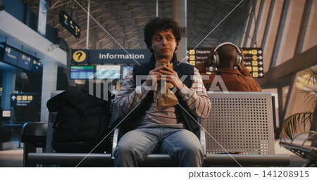 Young Male Traveler Eating Pastry and Waiting for Flight in Airport Lounge Young Male Traveler Eating Pastry and Waiting for Flight in Airport Lounge 141208915