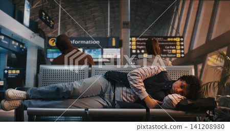 Tired Young Man Using Backpack as Pillow to Sleep on Airport Seats Tired Young Man Using Backpack as Pillow to Sleep on Airport Seats 141208980