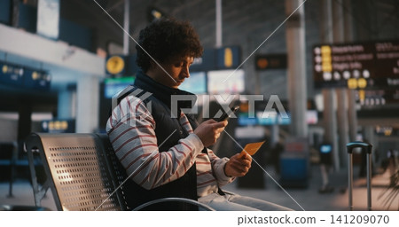 Young Man Sitting in Airport Terminal and Scanning Digital Ticket on Phone Young Man Sitting in Airport Terminal and Scanning Digital Ticket on Phone 141209070