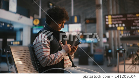 Young Man Sitting in Airport Terminal and Scanning Digital Ticket on Phone Young Man Sitting in Airport Terminal and Scanning Digital Ticket on Phone 141209104