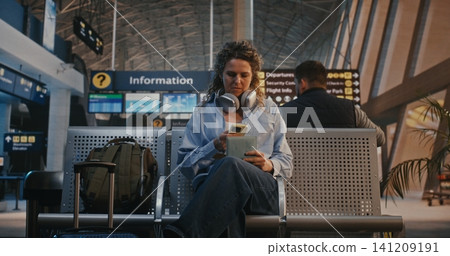 Young Woman Scanning Flight Ticket and Using Headphones and Scroll Social Media Young Woman Scanning Flight Ticket and Using Headphones and Scroll Social Media 141209191