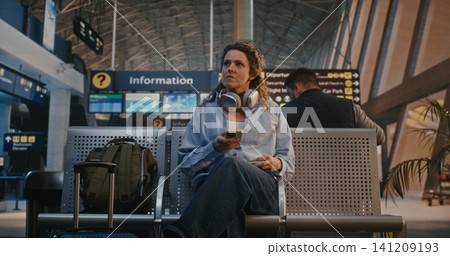 Young Woman Scanning Flight Ticket and Using Headphones and Scroll Social Media Young Woman Scanning Flight Ticket and Using Headphones and Scroll Social Media 141209193