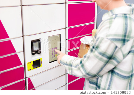 Man holding a package box while using a touch screen terminal at a contactless parcel locker for his online shopping delivery pickup. 141209933
