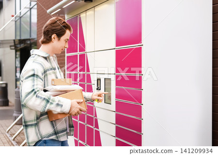 Man using a touch screen at a self-service parcel locker to collect packages, representing an efficient online shopping delivery service. Man using a touch screen at a self-service parcel locker to collect packages, representing an efficient online shopping delivery service. 141209934