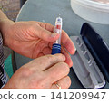 A person prepares an insulin pen for use, holding the medical device in their hands next to its carrying case. This tool is commonly used by individuals to manage blood glucose levels for diabetes 141209947