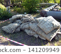 A pile of old, discarded mineral wool insulation lies on the grass near large industrial pipes. The area is cordoned off with safety tape, likely during maintenance work on the heating system 141209949