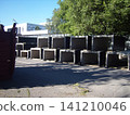 Rows of rectangular precast concrete elements are neatly stacked at a construction site. These heavy, hollow utility conduits sit on asphalt, ready for infrastructure development under a bright sky 141210046