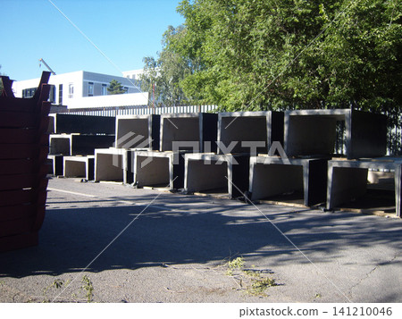 Rows of rectangular precast concrete elements are neatly stacked at a construction site. These heavy, hollow utility conduits sit on asphalt, ready for infrastructure development under a bright sky Rows of rectangular precast concrete elements are neatly stacked at a construction site. These heavy, hollow utility conduits sit on asphalt, ready for infrastructure development under a bright sky 141210046