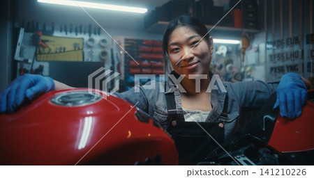 Female Rider Smiles While Repairing Motorcycle in Modern Garage Workshop Female Rider Smiles While Repairing Motorcycle in Modern Garage Workshop 141210226