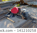 A heavy-duty red industrial rebar bending or cutting machine sits on a concrete site, surrounded by numerous stacks of steel rebar rods. The equipment appears ready for use in a construction projec 141210258