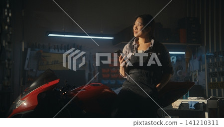 Young Biker Pauses in Modern Garage Checking Message on Smartphone Young Biker Pauses in Modern Garage Checking Message on Smartphone 141210311