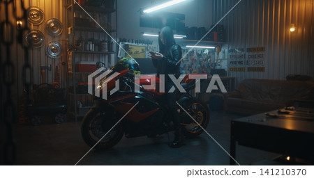 Stylish Woman in Leather Gear Using Phone Map While Sitting on Red Sport bike in Professional Garage Stylish Woman in Leather Gear Using Phone Map While Sitting on Red Sport bike in Professional Garage 141210370