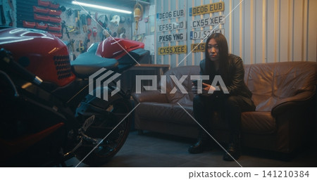 Focused Woman Sits on Couch, Holding Smartphone and Waiting For Signal to Start Journey Focused Woman Sits on Couch, Holding Smartphone and Waiting For Signal to Start Journey 141210384