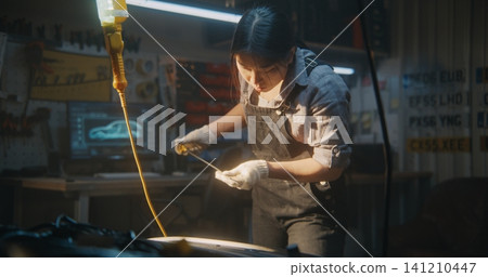 Female Auto Mechanic Checking Oil Level With Dipstick in Workshop 141210447