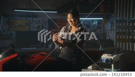 Young Woman Leans Casually Against Red Sport Motorcycle While Talking Friend on Video Call Young Woman Leans Casually Against Red Sport Motorcycle While Talking Friend on Video Call 141210453