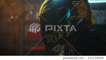 Young Woman Puts on Black Helmet With Green RIDE Graphics, Fastens Chin Strap, Lowers Visor 141210494