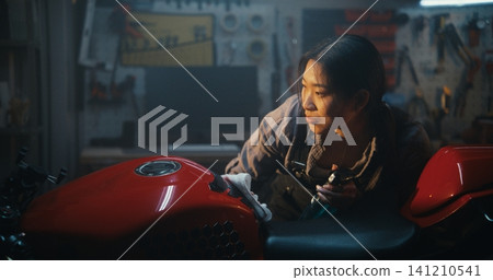 Smiling Female Mechanic Detailing Motorbike With Spray and Cloth on Sunny Day Smiling Female Mechanic Detailing Motorbike With Spray and Cloth on Sunny Day 141210541