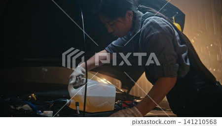 Professional Woman Auto Technician Refills Automotive Fluid Under Hood in Modern Workshop Professional Woman Auto Technician Refills Automotive Fluid Under Hood in Modern Workshop 141210568
