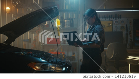 Woman Technician Stands Open Car Hood, Holding Laptop Connected Vehicle Onboard Computer System Woman Technician Stands Open Car Hood, Holding Laptop Connected Vehicle Onboard Computer System 141210619