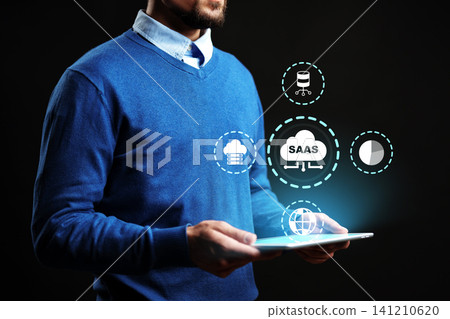Man holds tablet with SaaS graphics in dark setting while looking at clouds and data icons Man holds tablet with SaaS graphics in dark setting while looking at clouds and data icons 141210620