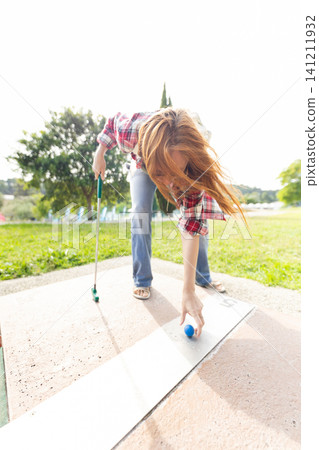 Girl rolls a ball on a putting green during a game in a park on a sunny day Girl rolls a ball on a putting green during a game in a park on a sunny day 141211932
