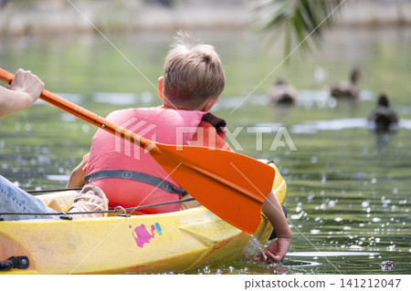 Child paddles a yellow kayak on a calm water body while ducks swim nearby Child paddles a yellow kayak on a calm water body while ducks swim nearby 141212047