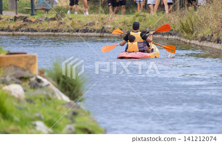 People are kayaking on a narrow waterway in a park area during the afternoon on a sunny day People are kayaking on a narrow waterway in a park area during the afternoon on a sunny day 141212074