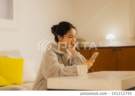 A young woman looking at her smartphone in the living room at night A young woman looking at her smartphone in the living room at night 141212745