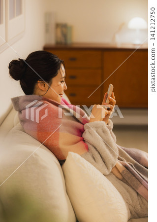 A young woman looking at her smartphone in the living room at night A young woman looking at her smartphone in the living room at night 141212750