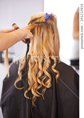 Back view, curls and hairdresser with curling iron for hair care, maintenance and styling for makeover. Balayage, waves and curly hairstyle, people and professional hairstylist at salon for beauty 141212914