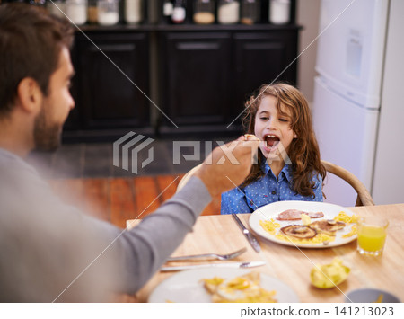 Dad, feeding and girl eating breakfast on table at home kitchen for health, nutrition and wellness. Child, father and happy for food in family house together for morning meal, development and diet Dad, feeding and girl eating breakfast on table at home kitchen for health, nutrition and wellness. Child, father and happy for food in family house together for morning meal, development and diet 141213023