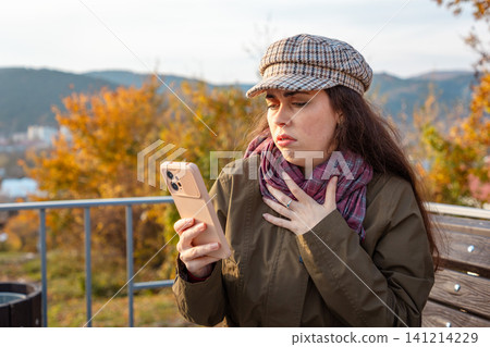 Woman touching cap with phone in hand Woman touching cap with phone in hand 141214229