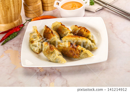 Fried dumplings on white plate with chili peppers and dipping sauce Fried dumplings on white plate with chili peppers and dipping sauce 141214912