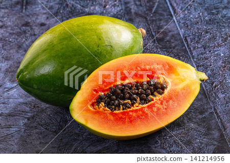 Fresh papaya whole and halved on dark textured surface Fresh papaya whole and halved on dark textured surface 141214956
