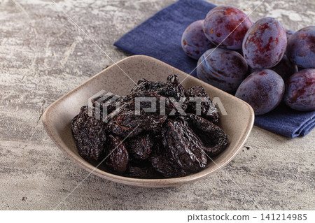 Dried plums in ceramic bowl with fresh plums on blue napkin Dried plums in ceramic bowl with fresh plums on blue napkin 141214985