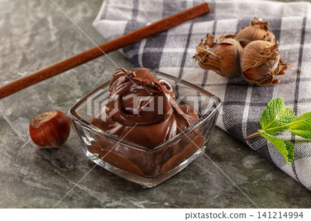 Rich chocolate spread in glass bowl with hazelnuts and mint on stone surface Rich chocolate spread in glass bowl with hazelnuts and mint on stone surface 141214994