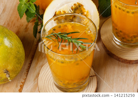 Passion fruit juice made with natural pulp, garnished with rosemary and whole passion fruits, set against a wooden background Passion fruit juice made with natural pulp, garnished with rosemary and whole passion fruits, set against a wooden background 141215250
