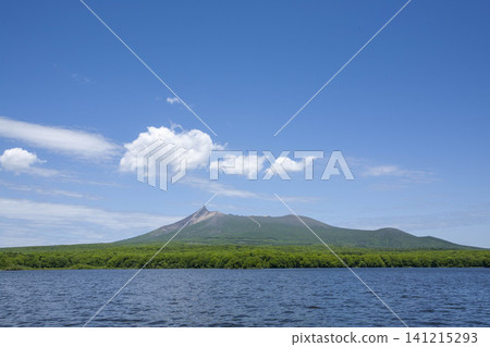 A view of the lush green Mount Hakodate from the sea, with the blue ocean and white clouds creating a stunning landscape. A view of the lush green Mount Hakodate from the sea, with the blue ocean and white clouds creating a stunning landscape. 141215293