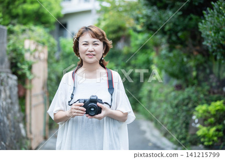 A middle-aged female photographer with a DSLR camera around her neck smiles and looks directly at the camera. 141215799