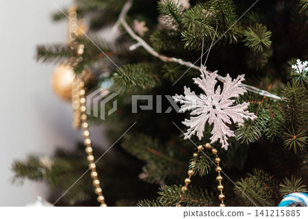 Glittering snowflake ornament on a decorated Christmas tree with festive lights and golden garland. Cozy winter holiday background for Christmas, New Year, celebration, seasonal greeting, and festive Glittering snowflake ornament on a decorated Christmas tree with festive lights and golden garland. Cozy winter holiday background for Christmas, New Year, celebration, seasonal greeting, and festive 141215885