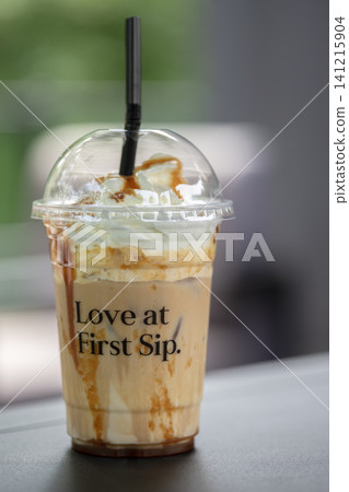 Eye-level vertical shot of an iced coffee with cream and caramel drizzle against a blurred outdoor backdrop Eye-level vertical shot of an iced coffee with cream and caramel drizzle against a blurred outdoor backdrop 141215904