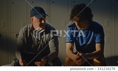 Supportive Coach Encouraging Sad Teenage Footballer in Locker Room Supportive Coach Encouraging Sad Teenage Footballer in Locker Room 141216276