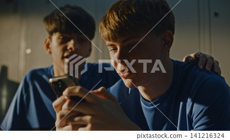 Teenage Footballers Looking at Smartphone and Talking in Locker Room Teenage Footballers Looking at Smartphone and Talking in Locker Room 141216324