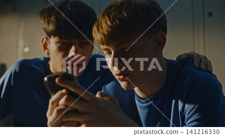 Teenage Footballers Looking at Smartphone and Talking in Locker Room Teenage Footballers Looking at Smartphone and Talking in Locker Room 141216330