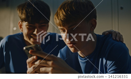 Teenage Footballers Looking at Smartphone and Talking in Locker Room Teenage Footballers Looking at Smartphone and Talking in Locker Room 141216331