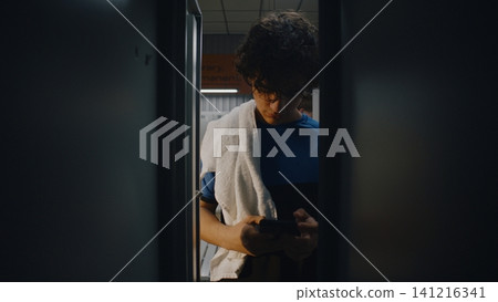 From Locker of Curly Haired Teen Athlete Checking Smartphone From Locker of Curly Haired Teen Athlete Checking Smartphone 141216341