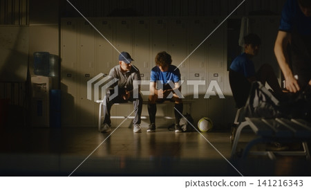 Lonely Teen Soccer Player Talking to Coach in Crowded Dressing Room Lonely Teen Soccer Player Talking to Coach in Crowded Dressing Room 141216343